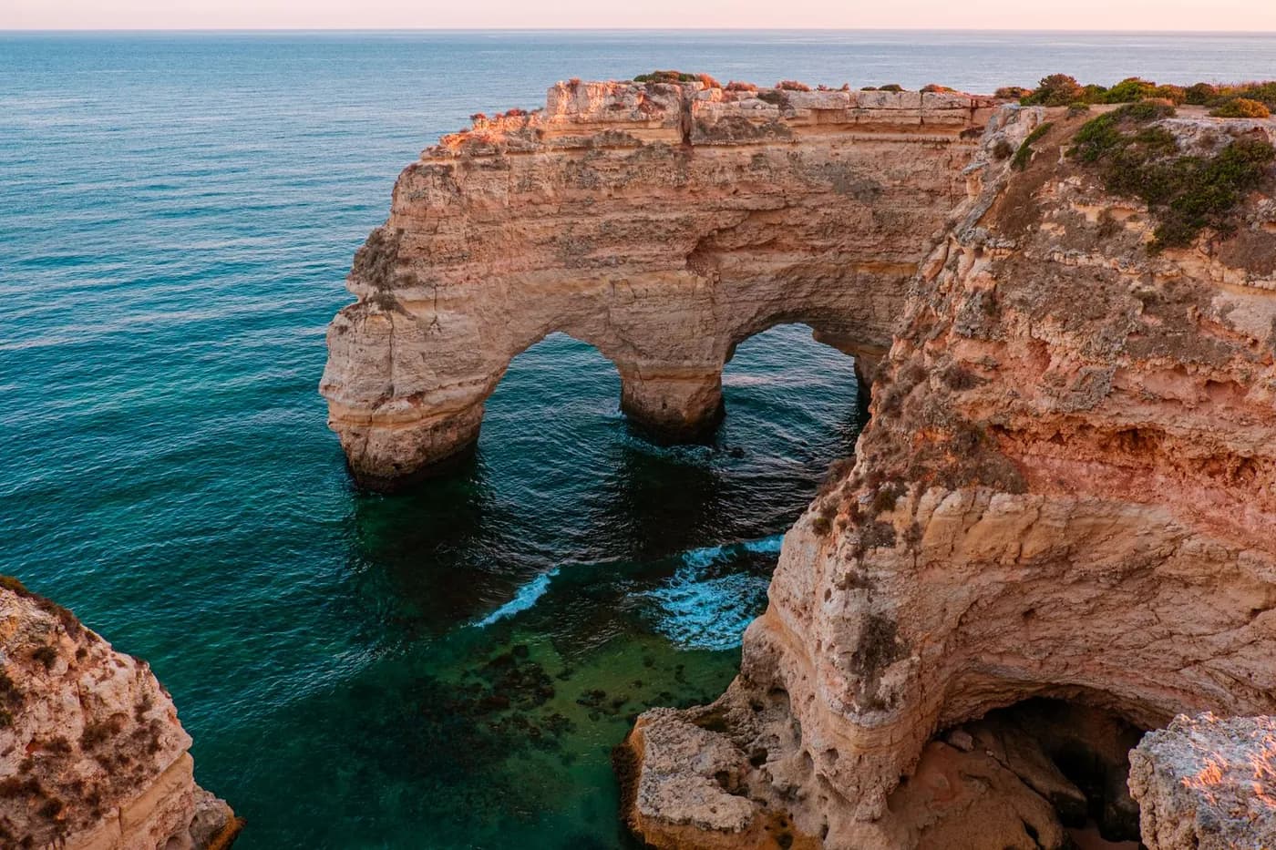 Falésias e um arco de rocha no mar, na costa algarvia, ao pôr do sol