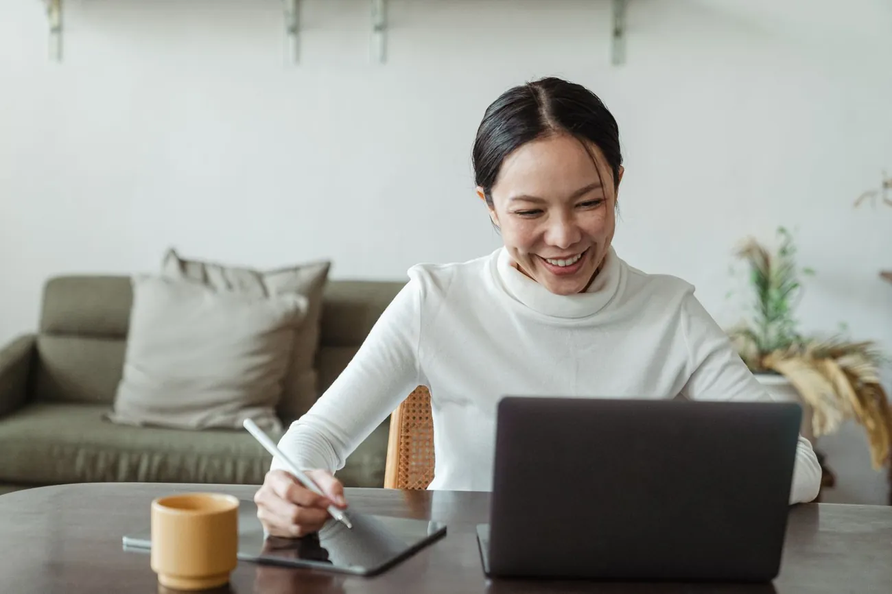 A woman taking notes during a video call at her laptop, at home